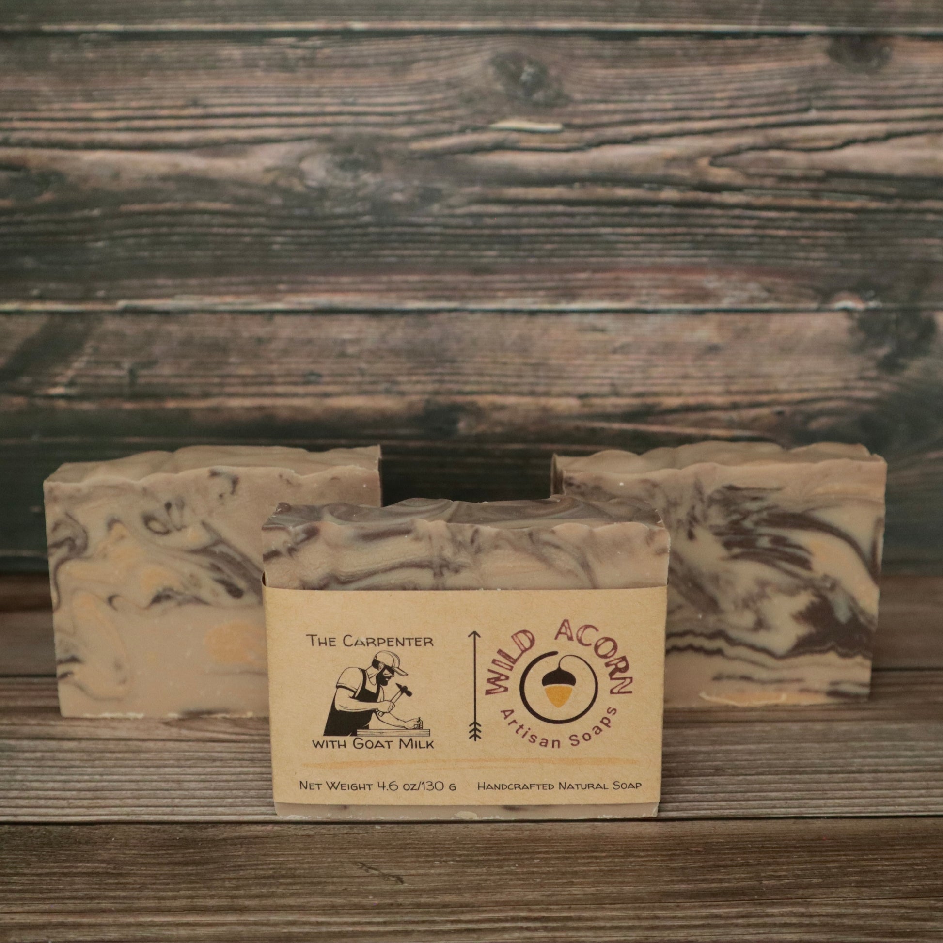 Three bars of soap with wood-colored swirls to resemble wood. One bar had a label on it with a picture of a man using a hammer to pound a nail. The background also looks like wood.