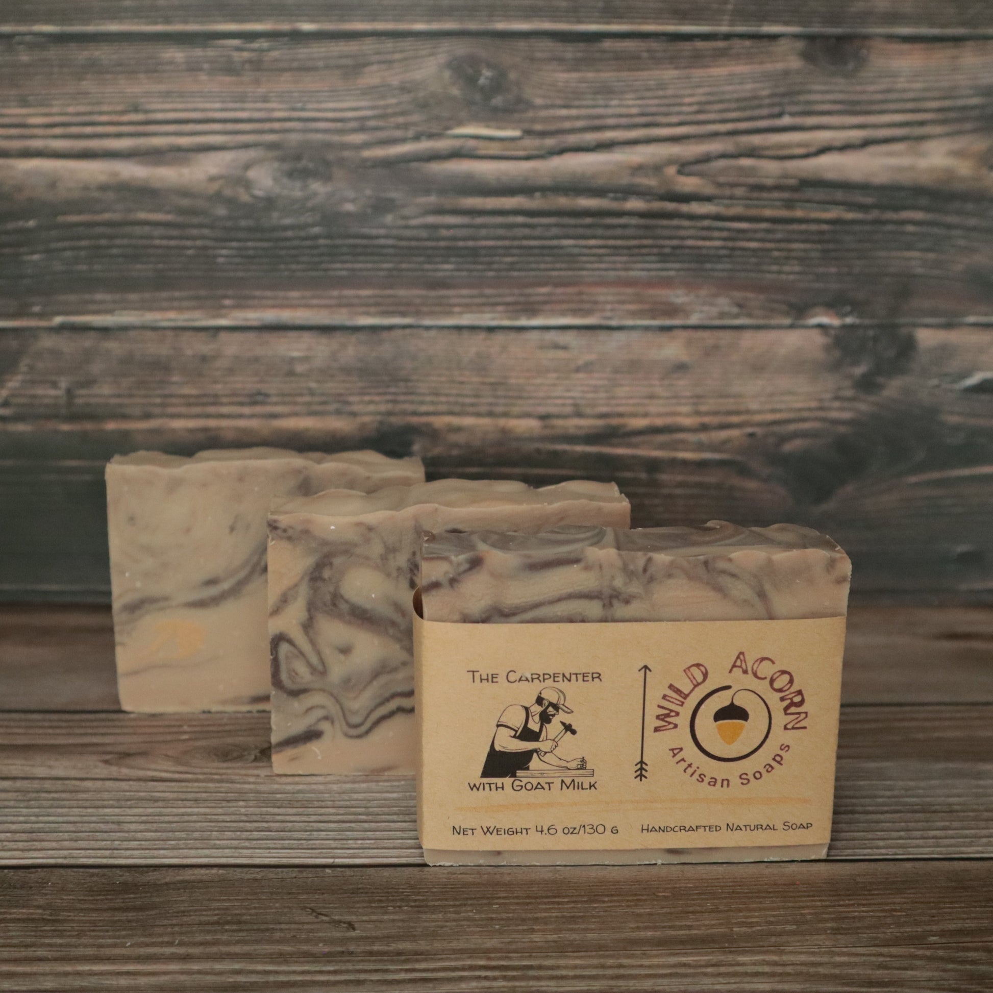 Three bars of soap with wood-colored swirls to resemble wood. One bar had a label on it with a picture of a man using a hammer to pound a nail. The background also looks like wood.